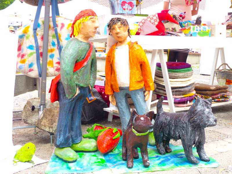 Bemalte Holzfiguren, ein Paar mit Hund, vor einem Marktstand