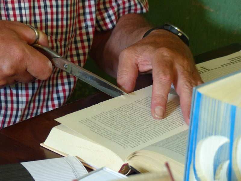 Buchfalten in Handarbeit, Hände mit Schere und aufgeschlagenem Buch